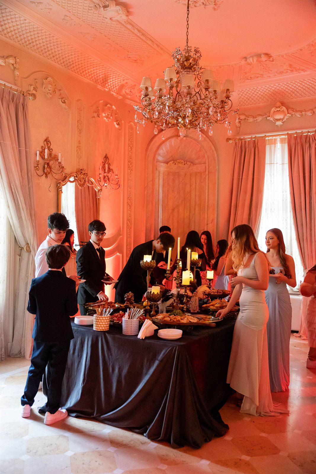 Invitați în ținute de gală în jurul bufetului sub candelabru de cristal la o petrecere de majorat la Palatul Noblesse