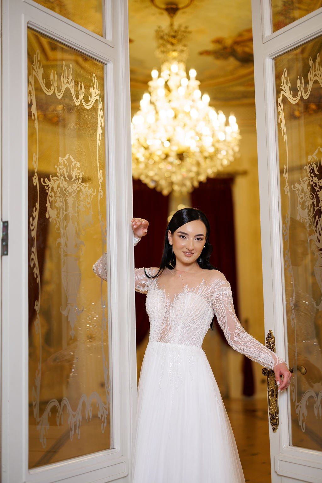 Mireasa Ioana în ușa Palatului Noblesse cu candelabrul de cristal — rochie dantelă și tulle