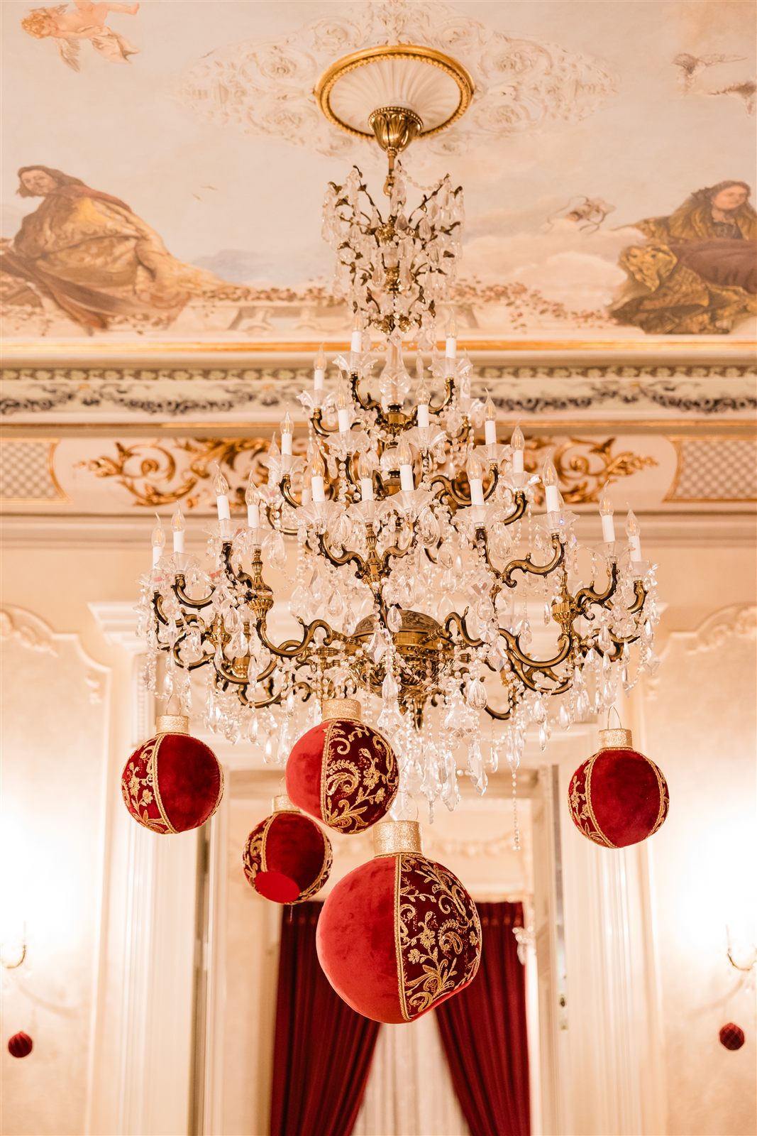 Candelabru de cristal cu globuri de catifea rosie sub tavanul pictat al Salonului Baroque la Palatul Noblesse