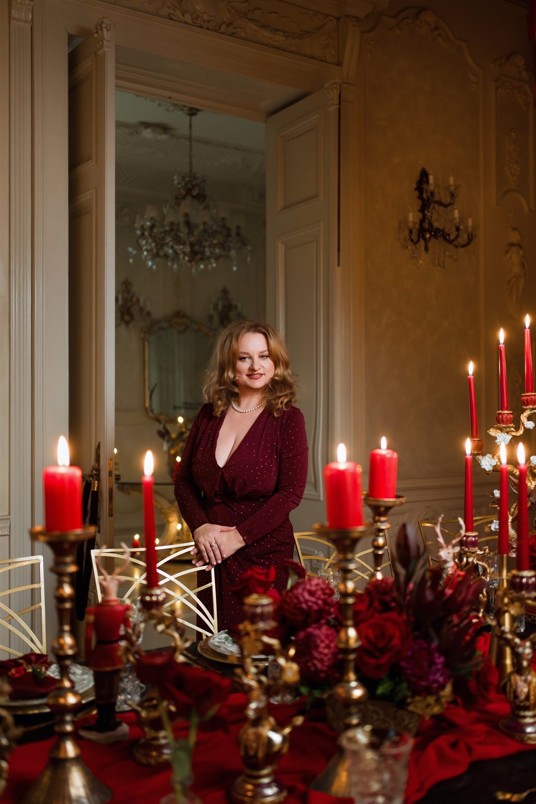 Gazdă elegantă în rochie roșie lângă masa de gală cu lumânări și candelabre la Palatul Noblesse