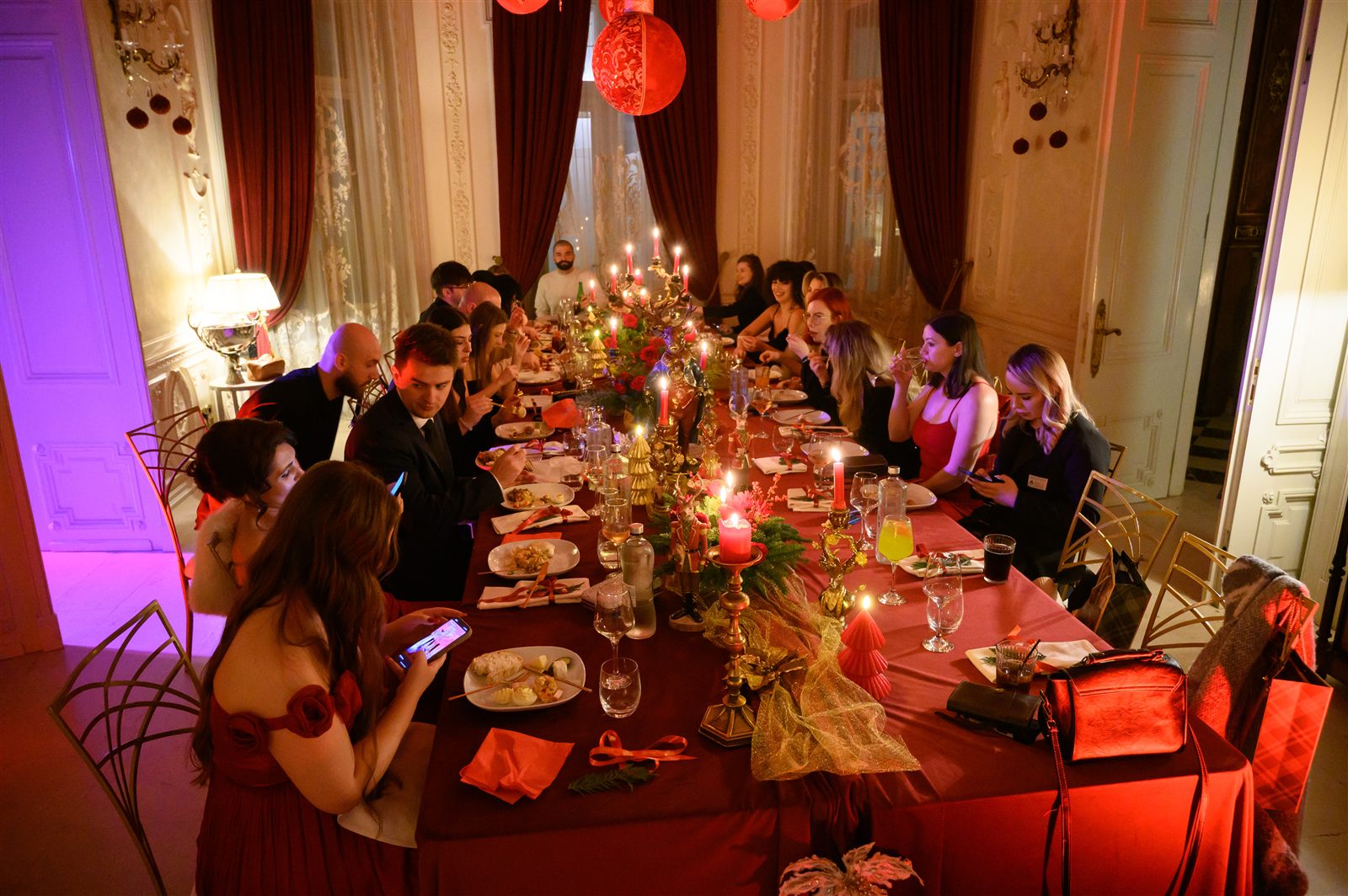 Invitații companiei la cina de Crăciun, la masa lungă din salonul cu plafon pictat
