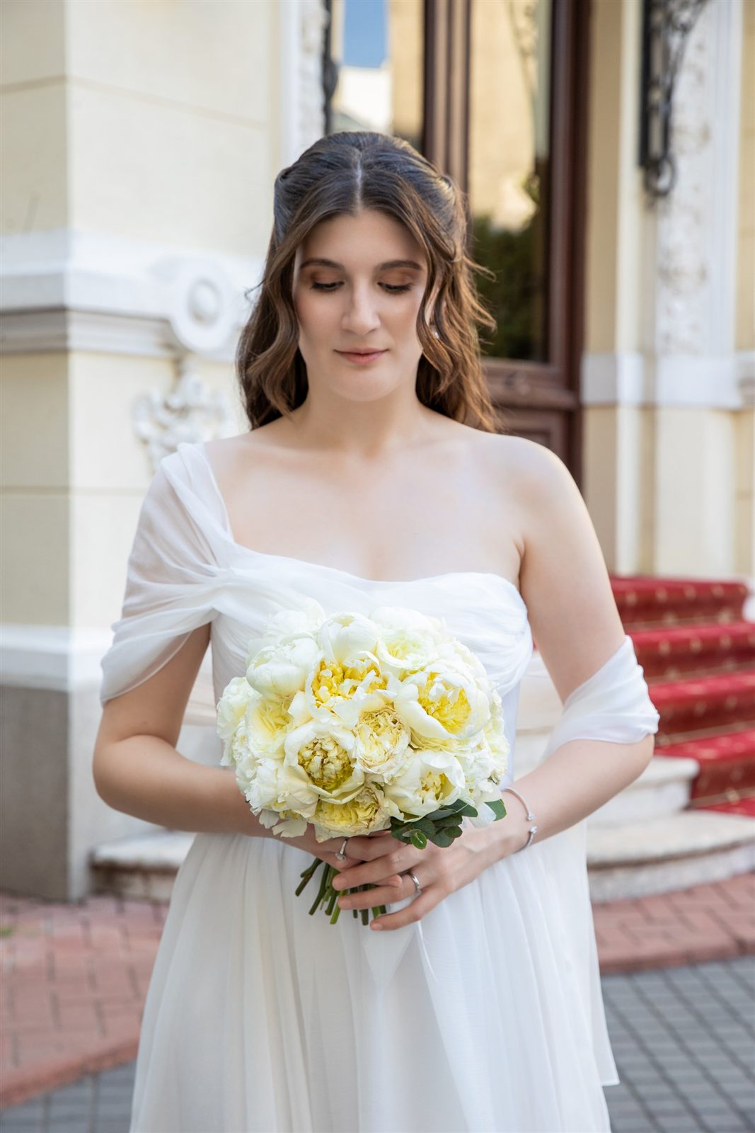 Portret de mireasă cu buchet de flori albe la fațada Palatului Noblesse — ședință foto de cununie