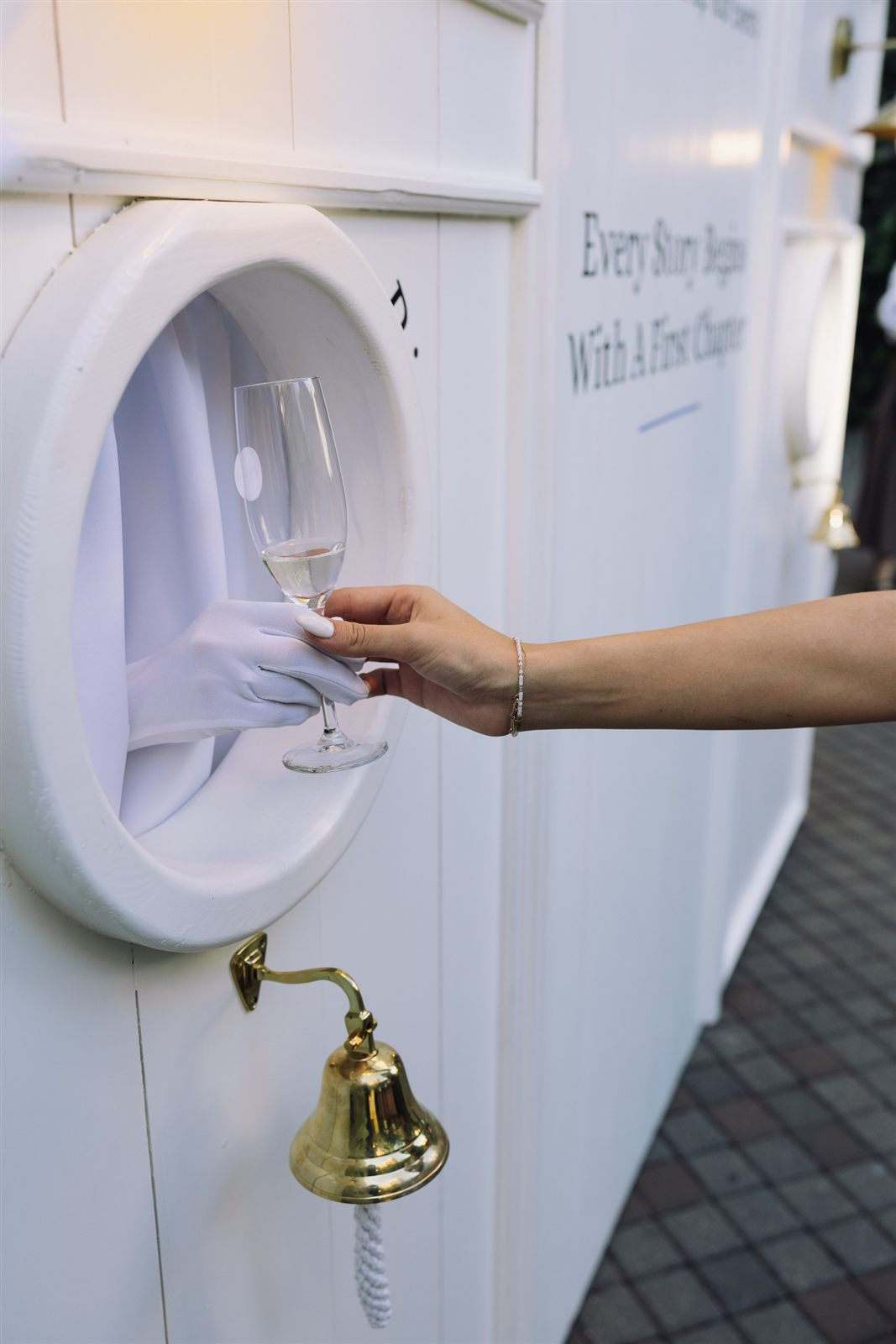 O mână servește un pahar prin fereastra rotundă, lângă clopoțel — Ring for Drinks Wall, Palatul Noblesse